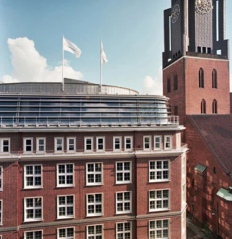Trotz ihrer zeitgemäßen, dynamischen und eher technischen Form nimmt sich die Fassade mit der klaren Linienführung dem alten Kontorhausviertel gegenüber zurück.